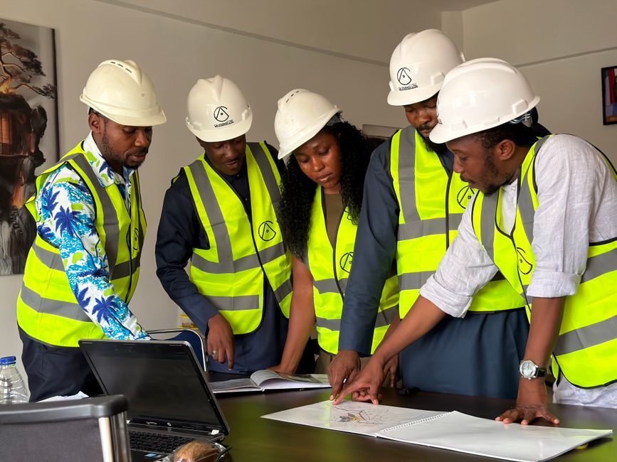 Group of engineers in safety gear reviewing blueprints indoors